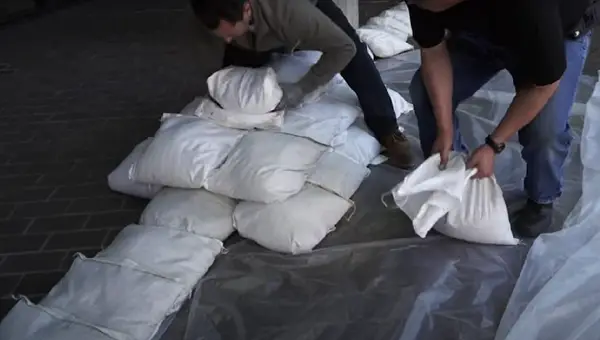 Two men placing white sand bags to protect a home from flood water. Image credit LA County Public Works.